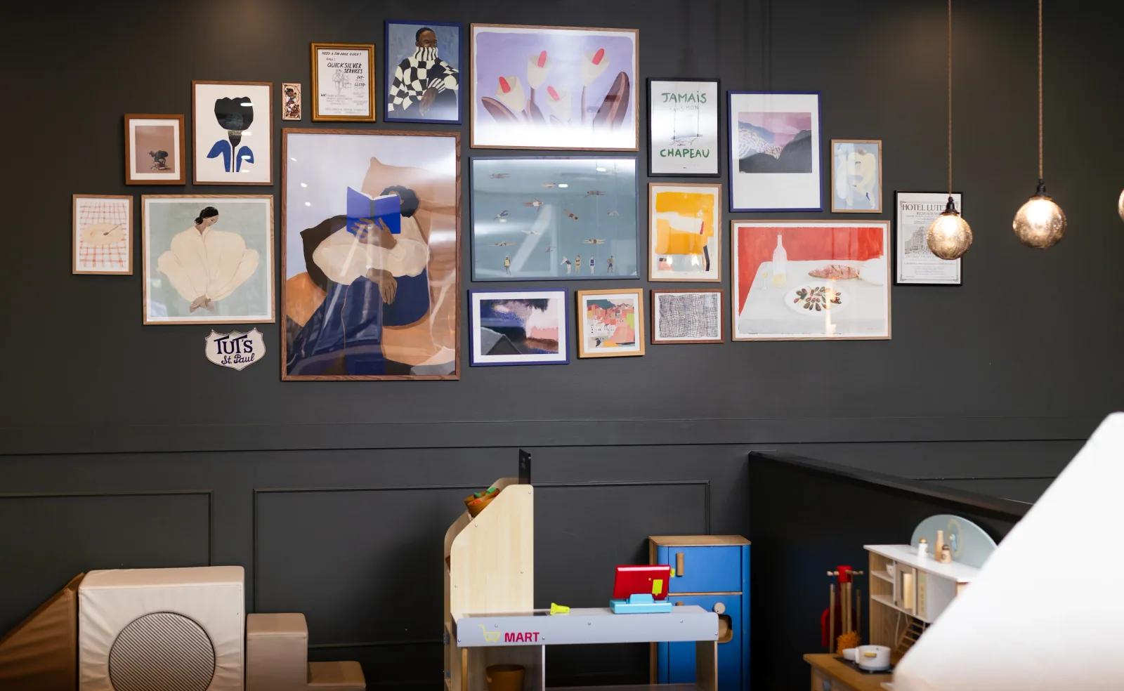 A framed art wall and children's play area inside The Den Family Social.